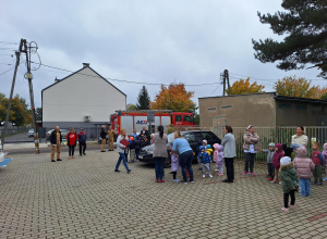 Zbiórka dzieci podczas próbnej ewakuacji przedszkola, w oddali widać wóz strażacki.